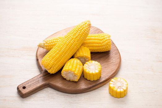 Sweet corn on cobs on cutting board on wooden table.