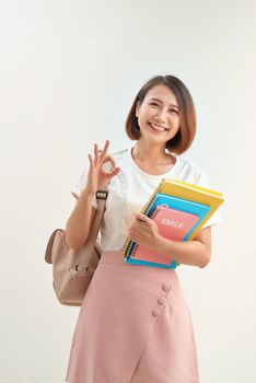 Portrait of a happy friendly girl student with backpack holding books and showing ok gesture isolated over white background