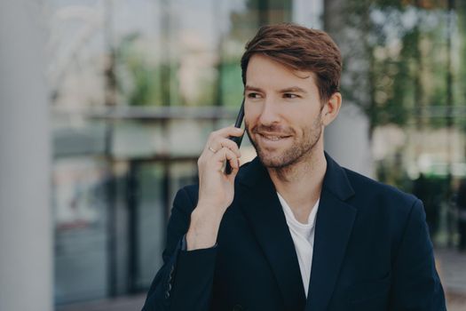 Handsome unshaven male executive worker left business building talks via smartphone