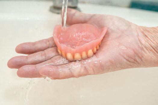 Asian senior or elderly old woman patient holding partial denture of replacement teeth.