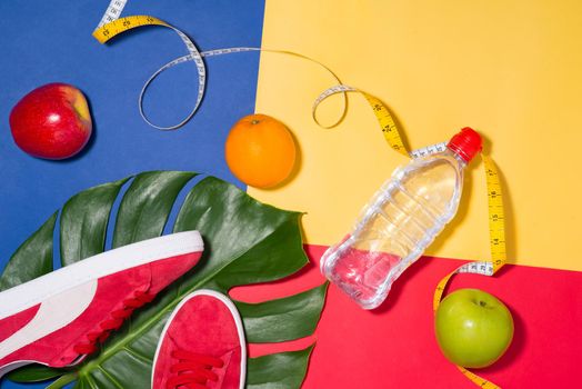 Sport concept. Fitness equipment. Sneakers, water, apple, dumbbell on colorful background.