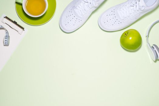 Fitness plan concept. Sneakers, tea, apple and headphone on pastel color background with open notebook.