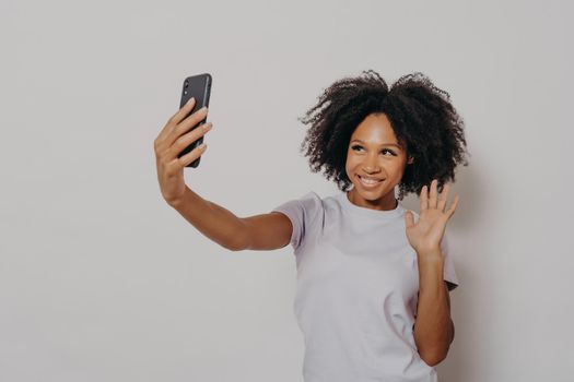 Happy young female waving at camera while having video call with best friend on modern smartphone