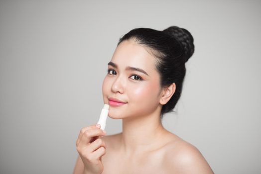 Asian woman applying hygienic lip balm over grey background