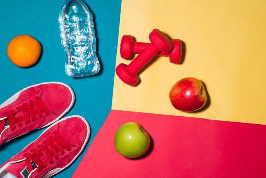 Sport concept. Fitness equipment. Sneakers, water, apple, dumbbell on colorful background.