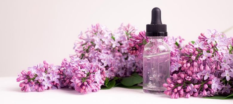 Hyaluronic acid bottle and lilac on a white background . Beauty container. Skin care. Vitamins for the skin. Rejuvenation. Female beauty. An article about the benefits of hyaluronic acid. Article about the choice of hyaluronate. Copy space. A branch of lilac. Flowering .