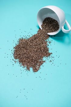 Nutritious chia seeds in cup on light blue background.