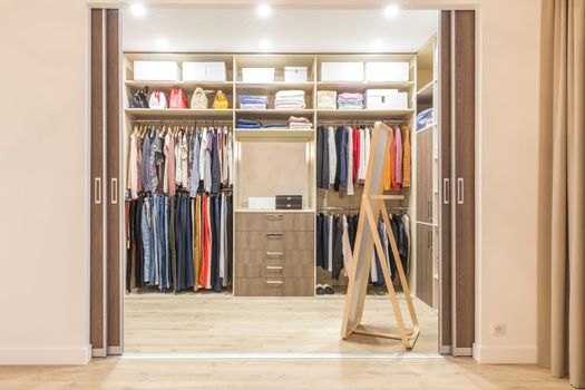 Modern wooden wardrobe with clothes hanging on rail in walk in closet