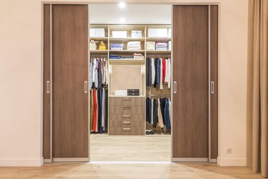 Modern wooden wardrobe with clothes hanging on rail in walk in closet