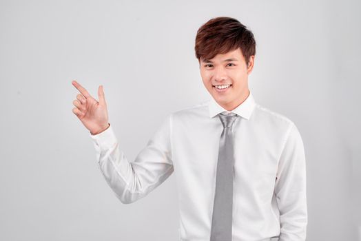 young casual student points finger to side on white background