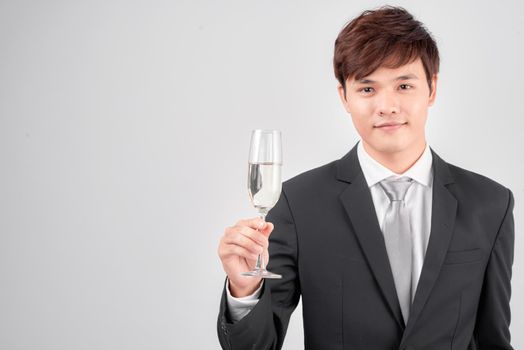 Handsome young businessman in suit and tie cheers with glass of champagne over white background