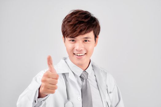 Positive asian male doctor in lab coat showing thumb up gesture over white background