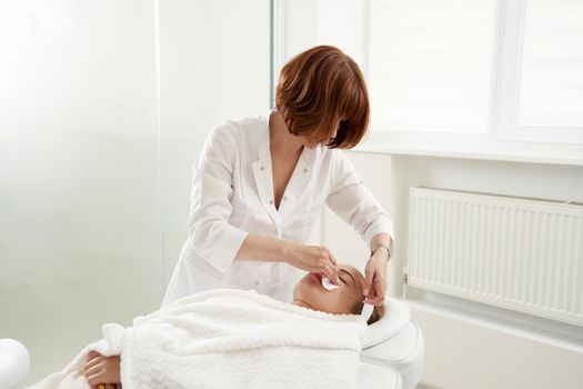Doctor puts needles into female face on the acupuncture treatment therapy in spa salon. Alternative Medicine concept