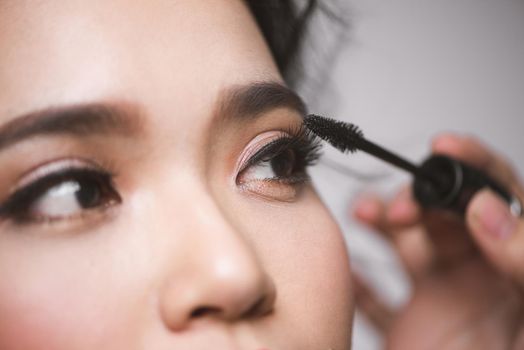 An asian woman applying mascara on her eyelashes