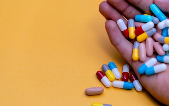 Hand holding colorful capsule pills on yellow background. Antibiotic drug overuse concept. Antibiotic drug resistance and superbug concept. Drug, vitamins, and supplements interactions. Prescription.