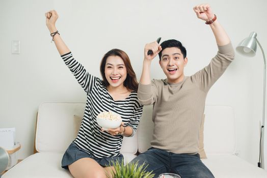 Excited young asian couple watching TV and eating popcorn