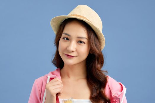Portrait of young Asian woman wearing hat, t-shirt, short jeans and pink jacket isolated over blue background.