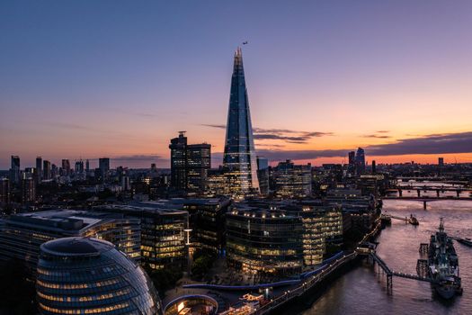 Aerial view of financial tower surrounded by small buildings in the beautiful city of London on a cloudy sunset evening with blue sky