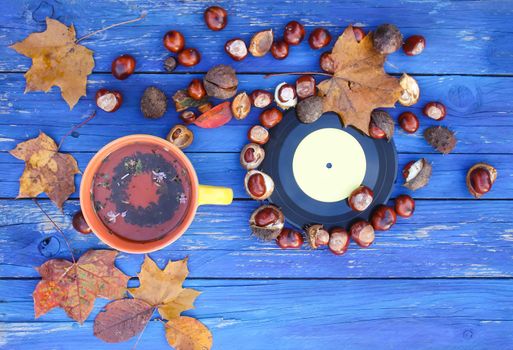 Yellow ceramic cup of herbal tea and vintage vinyl records on aged wooden background with fall autumn leaves and chestnuts.