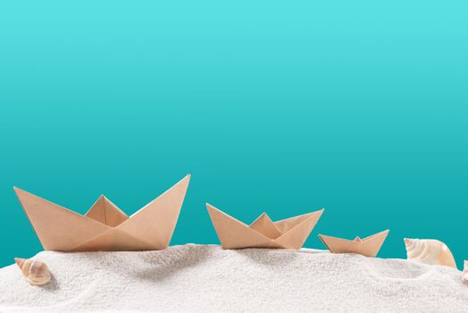 Boat paper origami on sand isolated on blue.
