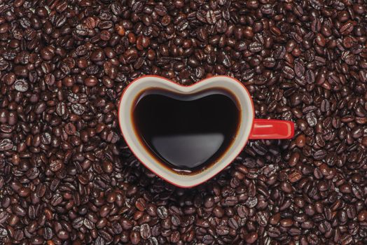 Red heart shape cup coffee on bean background