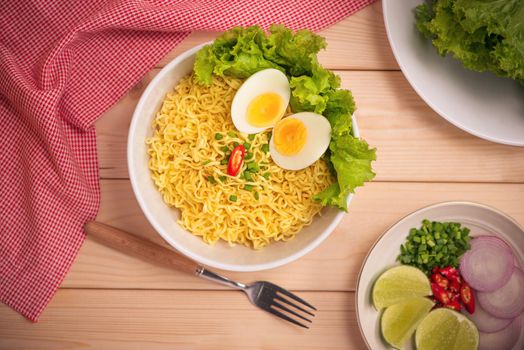 Instant noodles in bowl with vegetables and  boiled egg on wood background