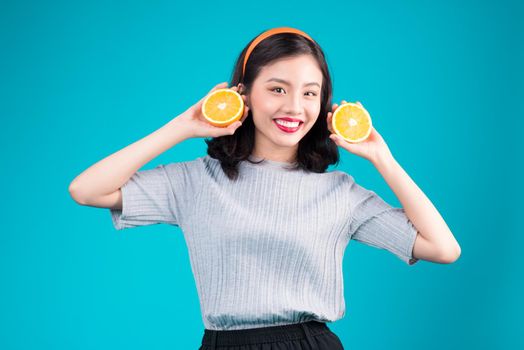 Healthy food. Smiling lovely pinup asian girl holding orange over blue background.