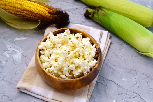 Tasty traditional popcorn and corn cobs on grey background