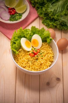 Instant noodles in bowl with vegetables and  boiled egg on wood background