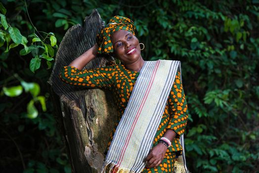 beautiful smiling african woman standing against a tree