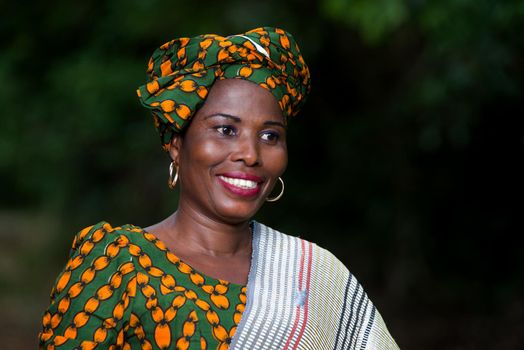 young african woman standing in traditional dress laughing while looking at the camera.