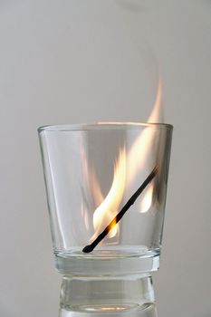 Remains of a dying match in a transparent glass on a light background.