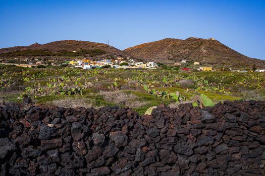 Characteristic view of dry stone wall built with lava stones. the town of Linosa on the background