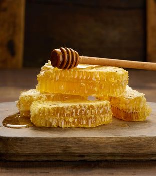 a stack of wax honeycombs with honey on a wooden board and a wooden spoon, brown table