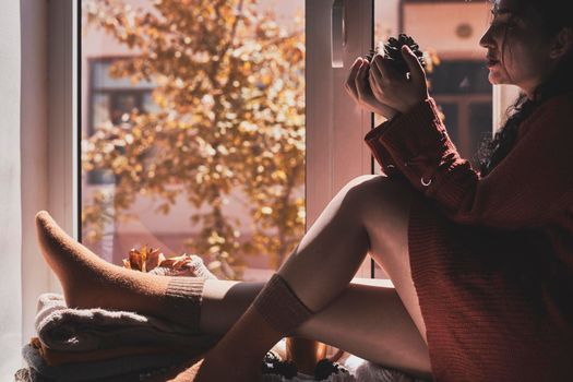 Cold autumn days - young multi-racial female drinks coffee in a cozy windowsill