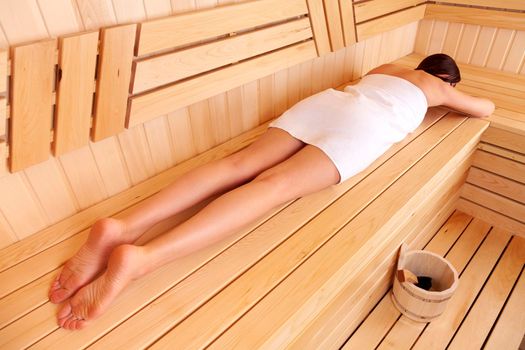 Woman relaxing in a traditional wooden sauna lying on her belly on the bench with a towel wrapped around her body