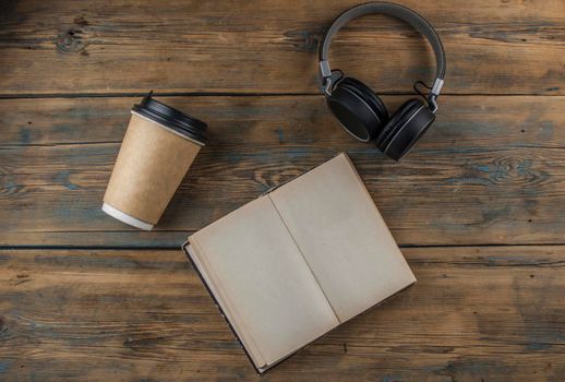 Open book  with blank page headphone and a cup of coffee in a disposable paper cup on a wooden table. Remote education concept. Top view