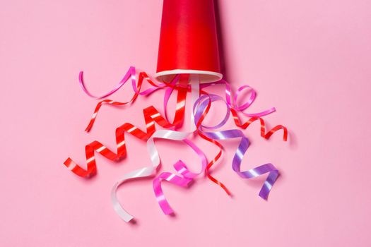 Flat lay of Celebration. Paper cup with colorful party streamers on pink background.