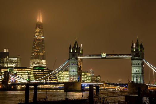 Tower Bridge and the Shard of London on a foggy evening with glowing lights.