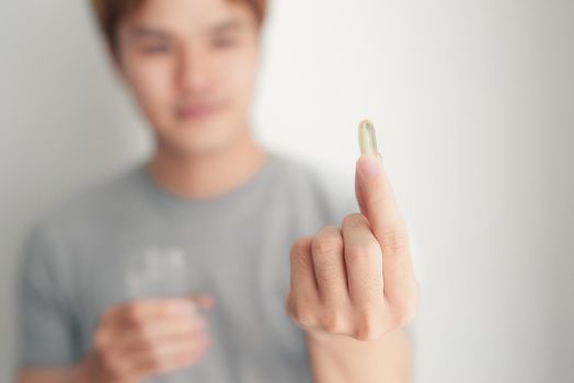 Blurred smiling handsome man holding omega 3 soft gel pill in his fingers