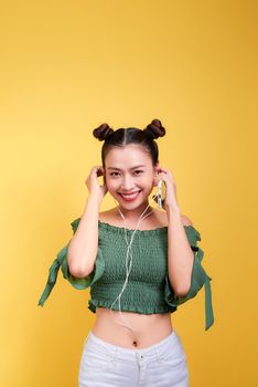Beautiful young asian woman in headphones listening to music and singing on yellow background
