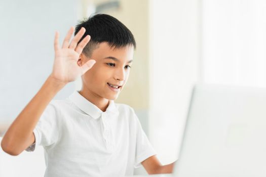 Boy using laptop to study and saying hi to teacher and classmate.