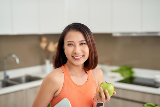 Asian woman holding apple and scale in the kitchen
