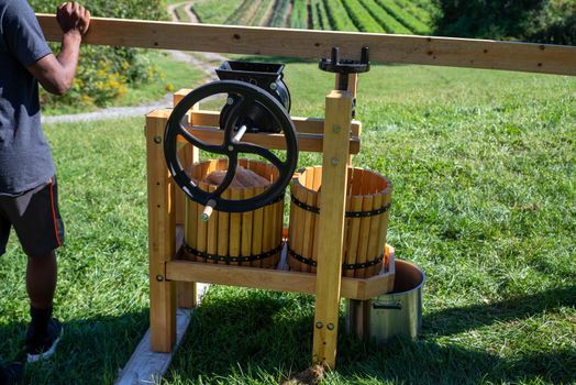 Young man turns crank on apple cider press with farm nature background