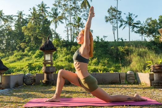 Young woman performing yoga asana at sunset with jungle background