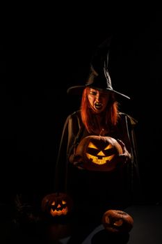 An evil witch holds a halloween jack-o-lantern glowing in the dark