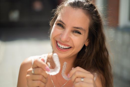 Beautiful caucasian woman holding transparent mouth guards for bite correction.