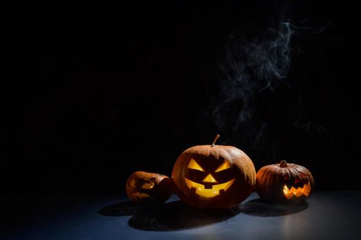 Pumpkins with carved grimaces and candles inside in the dark for halloween. Jack o latern in smoke.