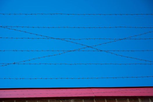 Barbed wire on the fence of the prison against the blue sky