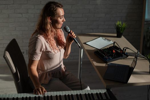 A female blogger sings and plays the live electronic piano. Portrait of a girl recording a song on a web camera and composing on a synthesizer. Online music lessons. Distance learning in quarantine.